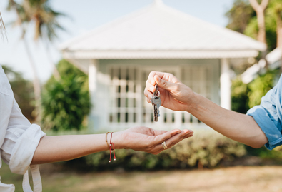 Man handing keys to woman in front of house